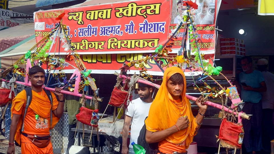 Kanwariyas walk past a shop on which banners with shopkeeper's name was put up on Kanwar Marg after an order issued by Uttar Pradesh Government, in Muzaffarnagar, Saturday, July 20, 2024.